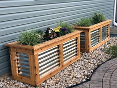 two wooden planters filled with plants next to a gray house and graveled walkway