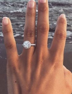 a woman's hand with a diamond ring on it and the ocean in the background