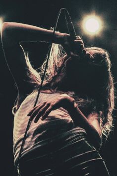 a woman holding a microphone up to her face while standing in front of a spotlight