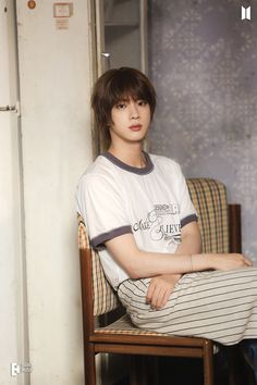 a young man sitting on top of a wooden chair next to a wall in a room