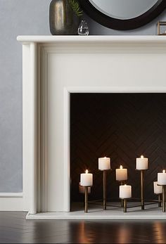 candles are lit in front of a fireplace with a mirror on the wall behind it