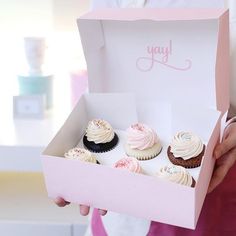 a person holding a pink box filled with cupcakes