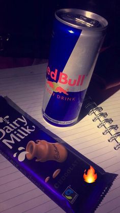 a can of red bull drink next to a chocolate bar with a lit candle on it