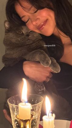 a woman holding a cat in her arms with two candles on the table behind her