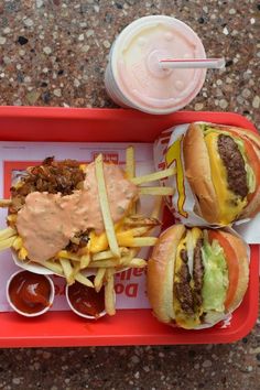 two hamburgers and fries with ketchup on a tray next to a drink