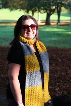 a woman wearing sunglasses and a yellow scarf stands in front of a tree with leaves on the ground