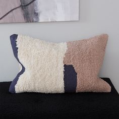 a pillow with two different colors on it sitting on top of a black shelf next to a painting