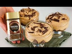 three desserts with chocolate frosting in small glasses on a green tray and a hand holding a jar