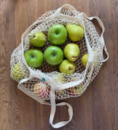 a bag filled with green apples on top of a wooden floor