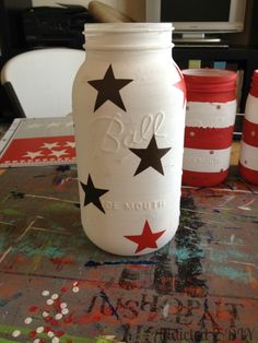 a painted mason jar sitting on top of a table next to two red and white striped jars