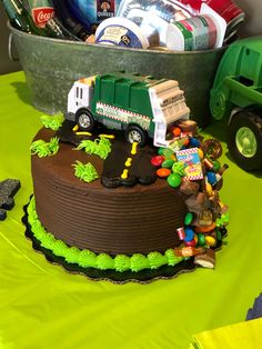 a birthday cake is decorated with toys and other items on a green tablecloth next to a dump truck