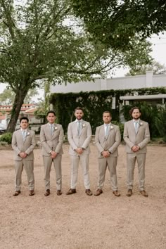 a group of men in suits standing next to each other on dirt ground near trees