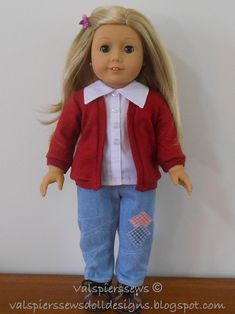 a doll with blonde hair wearing blue jeans and a pink cardigan top, standing on a wooden table