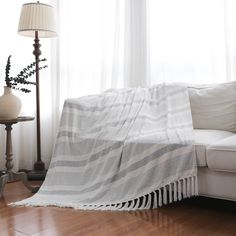 a white couch sitting next to a lamp on top of a hard wood floor covered in a blanket