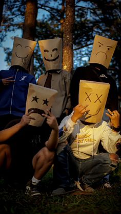 several people with paper bags on their faces are sitting in the grass and one person is holding something up to his face