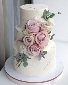 a three tiered wedding cake with pink flowers on the top and white frosting