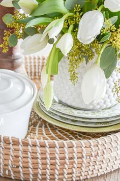 a white vase with flowers sitting on top of a wicker place mat next to a plate