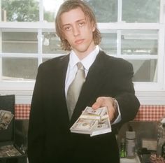 a man in a suit and tie is holding some money while standing in front of a window