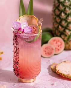 there is a pink drink in the glass with flowers on it and slices of fruit