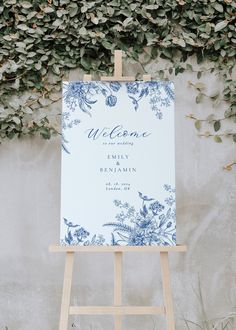 an easel with a welcome sign on it in front of a wall covered in greenery