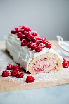 a cake roll with raspberries is on a cutting board