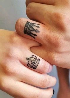 two people holding hands with tattoos on their fingers, one has a crown and the other has a cross