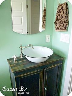 a bathroom sink sitting under a mirror next to a wooden cabinet with a white bowl on it