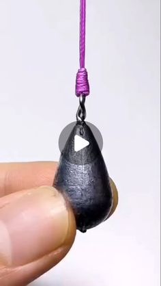 a hand holding a tiny black object with a purple cord