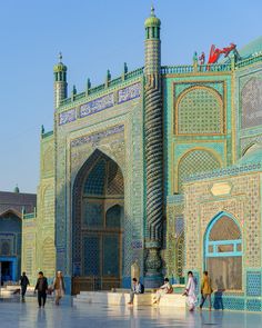 many people are walking around in front of a building with blue and green tiles on it