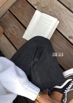 a person sitting on a bench with their legs crossed and reading a book in front of them