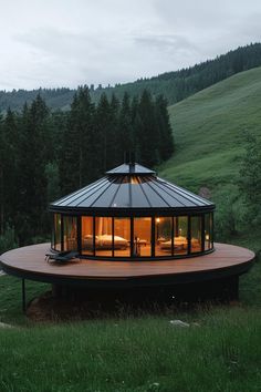 a round house in the middle of a grassy field with trees and hills behind it