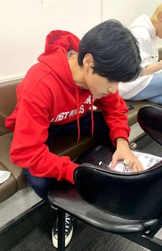 a young man sitting in a chair looking at his cell phone and writing on it