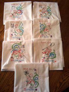 four embroidered napkins with different designs on them sitting on top of a wooden table