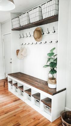 a white bench with baskets and hats on the wall above it, next to a potted plant