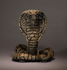 an intricately carved snake statue sitting on the ground in front of a gray background