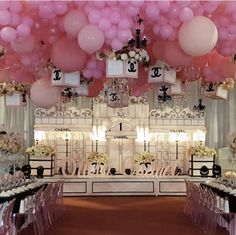 a room filled with lots of balloons and tables covered in white table cloths next to a chandelier