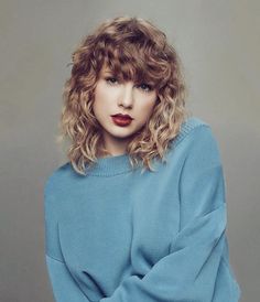 a woman with curly hair wearing a grey sweater and red lipstick is posing for the camera