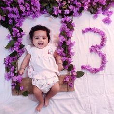 a baby is laying down in front of purple flowers that spell out the word love