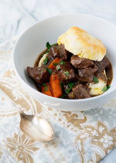 a bowl filled with meat and vegetables on top of a table next to a spoon