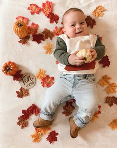 a baby is laying on the floor with autumn leaves around him and holding a piece of food