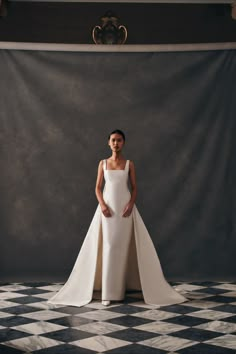 a woman standing in front of a black and white checkered backdrop wearing a wedding dress