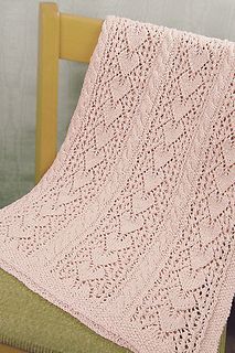 a pink knitted blanket sitting on top of a wooden chair next to a green pillow