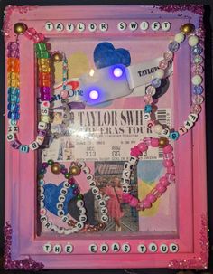 a pink frame with beads and other items in it that are attached to the wall