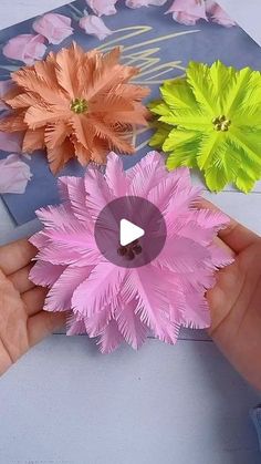 someone is holding three paper flowers in their hand, with one being held up to the camera