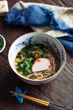 a bowl filled with noodles and vegetables next to chopsticks on a wooden table