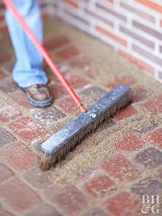 a person with a brush on the ground near a brick wall and red tile floor