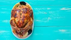 a roasted turkey with lemons and blueberries on a plate against a turquoise background