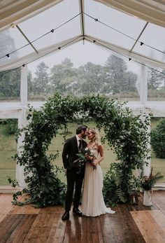 a bride and groom standing in front of an arch with greenery at their wedding