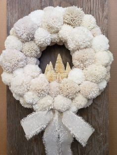 a wreath with white pom - poms hanging on a wooden door