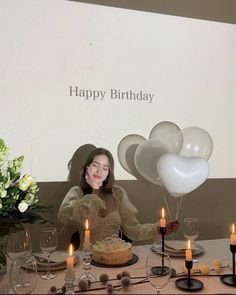 a woman sitting at a table with balloons and cake in front of her, surrounded by candles